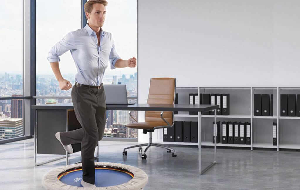 Mann beim Trampolintraining im Büro auf einem Trimilin-med Minitrampolin